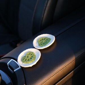 Pair of white and green crochet car coasters with Monstera leaf design on a car center console.
