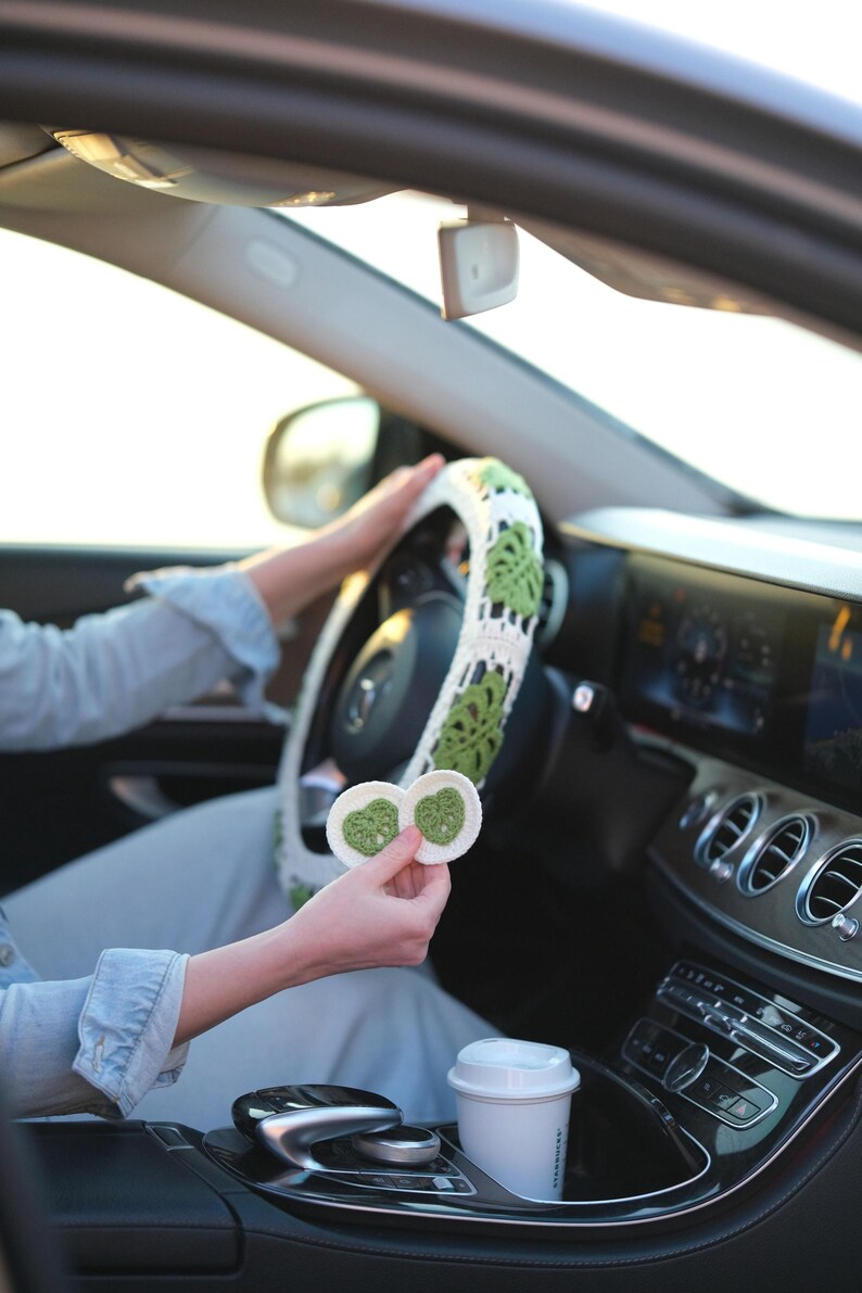 Monstera crochet steering wheel cover in a car while matching green and white crochet coasters are held in hand.