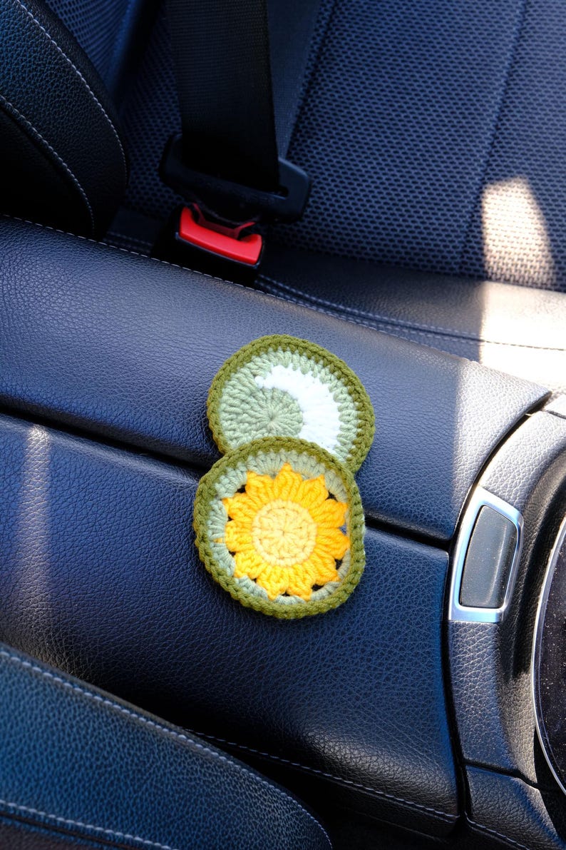 May include: Two handmade crochet coasters. One features a yellow sunflower design with a green border, and the other has a white swirl on a green background. These decorative coasters are perfect for protecting surfaces from drink condensation.