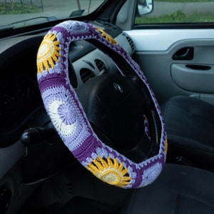 May include: A purple and yellow crocheted steering wheel cover with a sun and moon design.