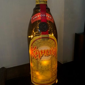 May include: A brown glass bottle with a red label that says "IMPORTED" and "Kahlua Licor Delicioso Liqueur". The bottle is lit up with string lights.