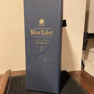 May include: A blue box with gold lettering for Johnnie Walker Blue Label Blended Scotch Whisky. The box features a gold crest and the text "A blend of our rarest whiskies" and "John Walker & Sons".
