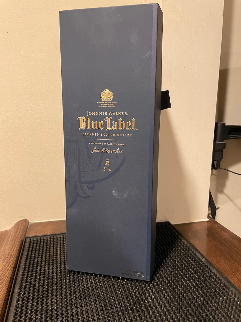 May include: A blue box with gold lettering for Johnnie Walker Blue Label Blended Scotch Whisky. The box features a gold crest and the text "A blend of our rarest whiskies" and "John Walker & Sons".