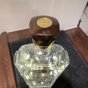 May include: A clear glass bottle with a brown and gold cap. The cap has a gold circle with the number "21" on it.