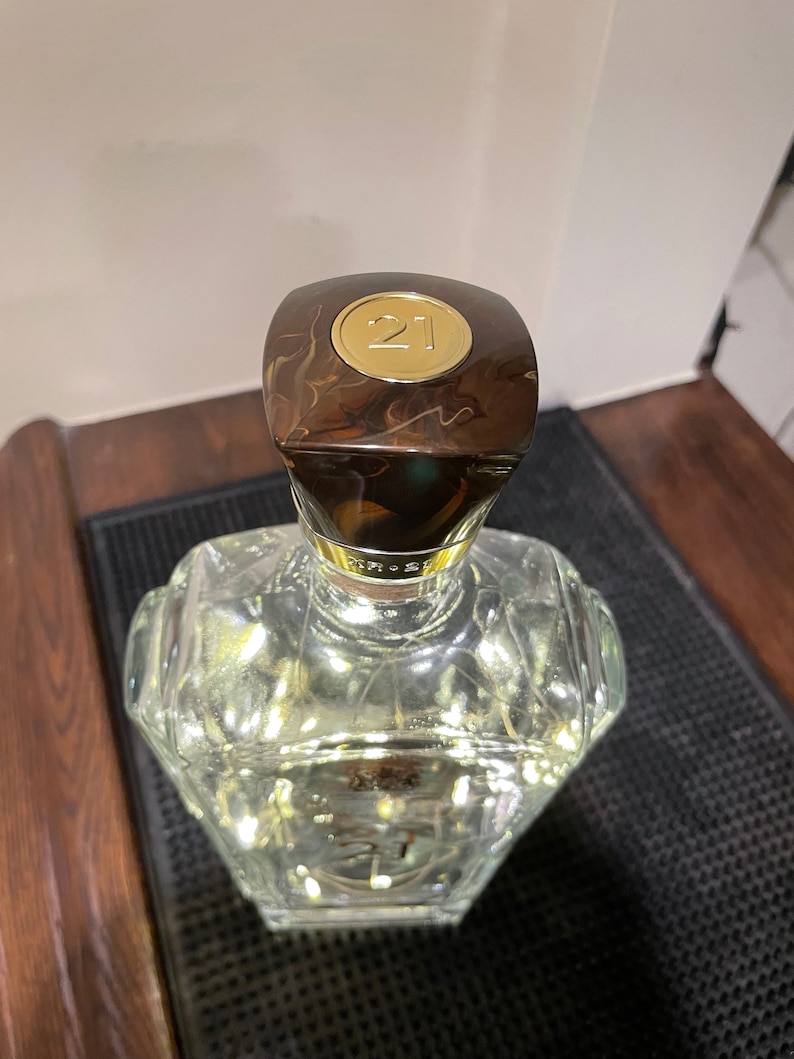 May include: A clear glass bottle with a brown and gold cap. The cap has a gold circle with the number "21" on it.