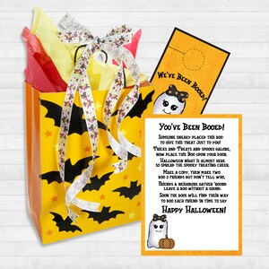 May include: A yellow and orange gift bag with black bats and stars printed on it. The bag is tied with a white and pink ribbon. A ghost-shaped card with the text "You've Been Booed!" is attached to the bag. The card has a ghost with a bow and a pumpkin on it. The text on the card reads: "Someone sneaky placed this boo to give this treat just to you! Tricks and treats and spooks galore, now place this boo upon your door. Halloween night is almost here so spread the spooky treating cheer. Make a copy, then make two, boo 2 friends but don't tell who. Friends and neighbors gather 'round leave a boo without a sound. Soon the boos will find their way to boo each friend in time to say Happy Halloween!"
