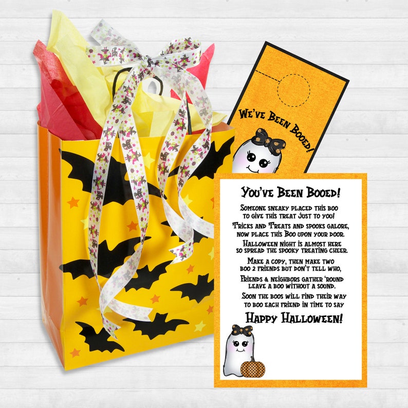 May include: A yellow and orange gift bag with black bats and stars printed on it. The bag is tied with a white and pink ribbon. A ghost-shaped card with the text "You've Been Booed!" is attached to the bag. The card has a ghost with a bow and a pumpkin on it. The text on the card reads: "Someone sneaky placed this boo to give this treat just to you! Tricks and treats and spooks galore, now place this boo upon your door. Halloween night is almost here so spread the spooky treating cheer. Make a copy, then make two, boo 2 friends but don't tell who. Friends and neighbors gather 'round leave a boo without a sound. Soon the boos will find their way to boo each friend in time to say Happy Halloween!"