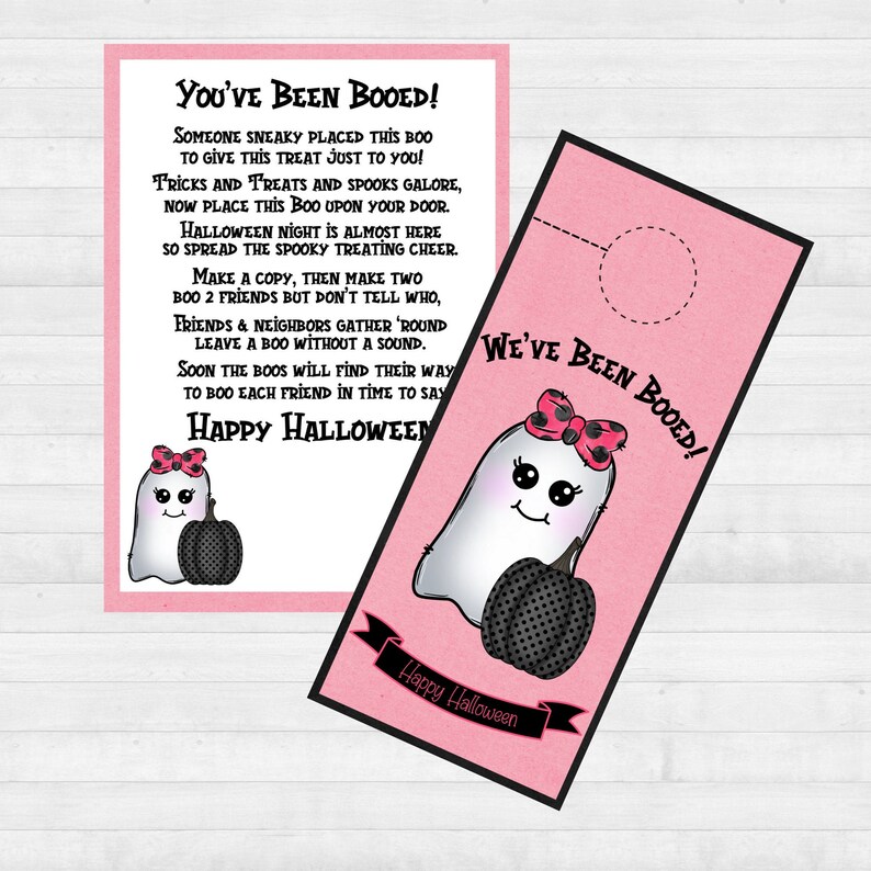 May include: A pink and white door hanger with a ghost holding a pumpkin. The text on the hanger reads "You've Been Booed!" and "We've Been Booed!" with a happy Halloween message at the bottom.