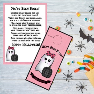 May include: Pink Halloween door hanger with a ghost holding a pumpkin. The text on the hanger reads "You've Been Booed!" and "We've Been Booed!" with a happy Halloween greeting at the bottom.