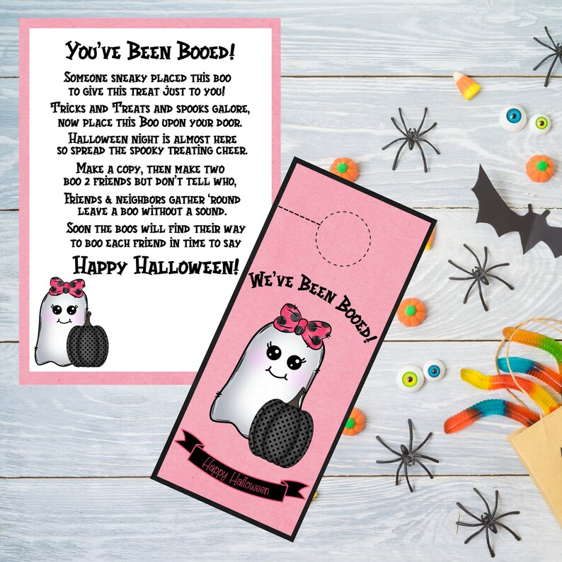May include: Pink Halloween door hanger with a ghost holding a pumpkin. The text on the hanger reads "You've Been Booed!" and "We've Been Booed!" with a happy Halloween greeting at the bottom.