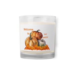May include: A glass candle holder with a white label featuring the text "Welcome to our patch!" and a watercolor illustration of three pumpkins and fall leaves. The pumpkins are orange, tan, and gray.