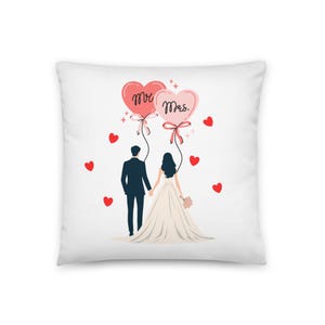 May include: White square pillow featuring a wedding-themed illustration. A couple is depicted holding hands, with heart-shaped balloons that read "Mr." and "Mrs." floating above them. Red hearts are scattered around the couple.
