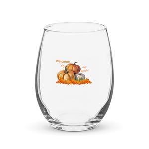 May include: A clear, stemless wine glass with a seasonal design. The image shows three pumpkins in orange and white, with orange leaves. The text "Welcome to our patch!" is printed above the pumpkins, perfect for autumn.