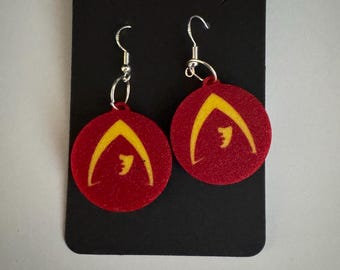 May include: A pair of red circular earrings with a yellow symbol. The earrings are hanging from silver hooks.