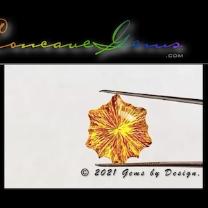 May include: A close-up of a yellow and orange gemstone with a starburst pattern. The gemstone is held by tweezers on a white background. The text "© 2021 Gems by Design." is visible in the bottom right corner of the image.