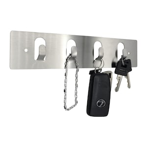 May include: A stainless steel key rack with four hooks. A car key, a chain, and two keys are hanging on the hooks.