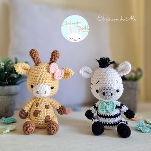Pode incluir: Dois animais de peluche de crochê, uma girafa e uma zebra, estão sentados em uma superfície branca. A girafa é amarela com manchas marrons e um laço rosa. A zebra é branca com listras pretas e uma gravata borboleta turquesa. O texto "El rincón de Ale" é visível no fundo.