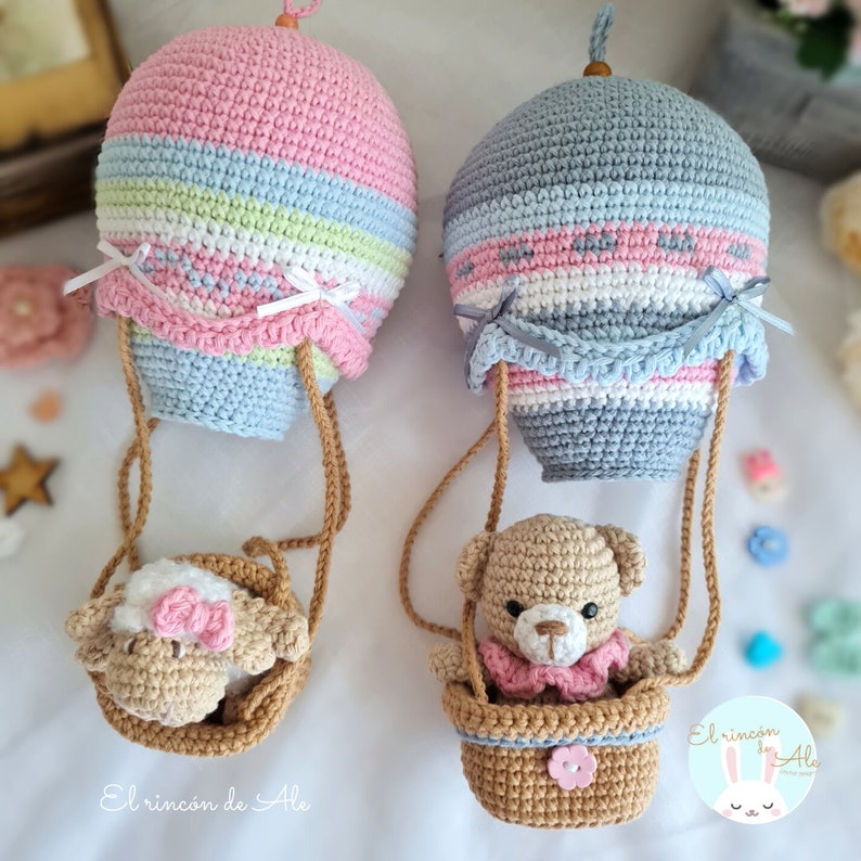 May include: Two crocheted hot air balloons with a teddy bear and a lamb in baskets hanging from the balloons. The balloons are striped in pink, blue, white, and green. The text "El rincon de Ale" is visible in the image.