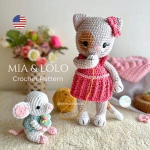Puede incluir: Patrón de crochet para Mia & Lolo, una gata gris y blanca con un vestido rosa y un ratón gris y blanco que sostiene una flor rosa. El patrón está disponible para su compra.