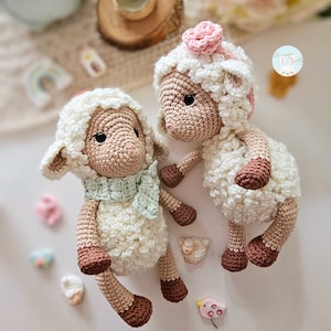 Puede incluir: Dos peluches de oveja blancos de crochet con patas y narices marrones. Una oveja tiene una flor rosa en la cabeza y una bufanda verde alrededor del cuello.