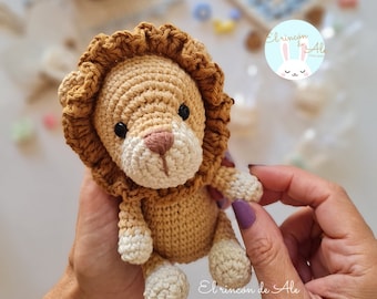 Puede incluir: Un juguete de león de crochet con una melena marrón y una cara blanca. El león sostiene una pequeña flor blanca en su pata.