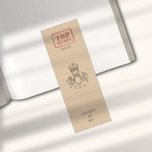 May include: A tan bookmark with a red "TOP SECRET" stamp and the text "B.S.I.S."  The bookmark also features a black and white illustration of a crown and two lions with the text "PROPERTY OF MIG".