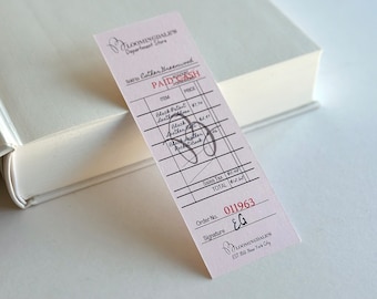 May include: A Bloomingdale's receipt with handwritten details, including "PAID CASH" and item descriptions like "Black Patent Leather Gloves." The receipt is pink with black text and rests on a white book.