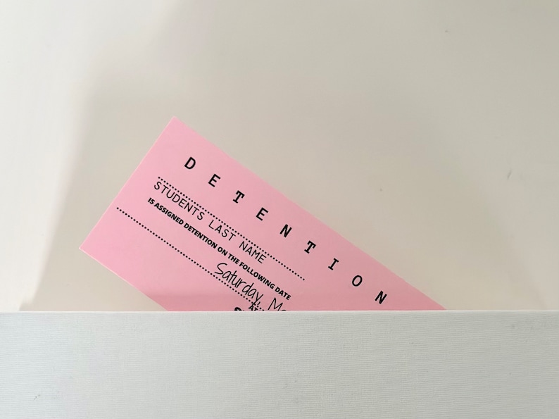 以下が含まれることがあります： ピンク色の留置票で、上部に「DETENTION」と、その下に「STUDENT'S LAST NAME」と書いてあります。この票には、生徒の姓と留置日の記入欄があり、日付欄には「Saturday, May」と記入されています。