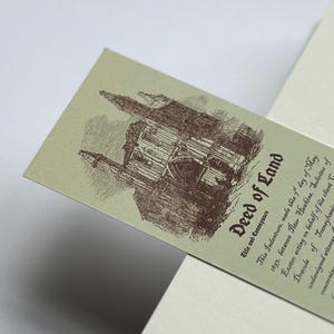 May include: A vintage-style bookmark with the title "Deed of Land" in a serif font. The bookmark features an illustration of a castle in brown ink on a light green background. Text details the conveyance.