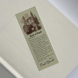 May include: A vintage-style bookmark with the text "Deed of Land" and an illustration of a building. The bookmark is rectangular, with a cream background and sepia-toned graphics and text. The text includes the signature "Count Dracula."