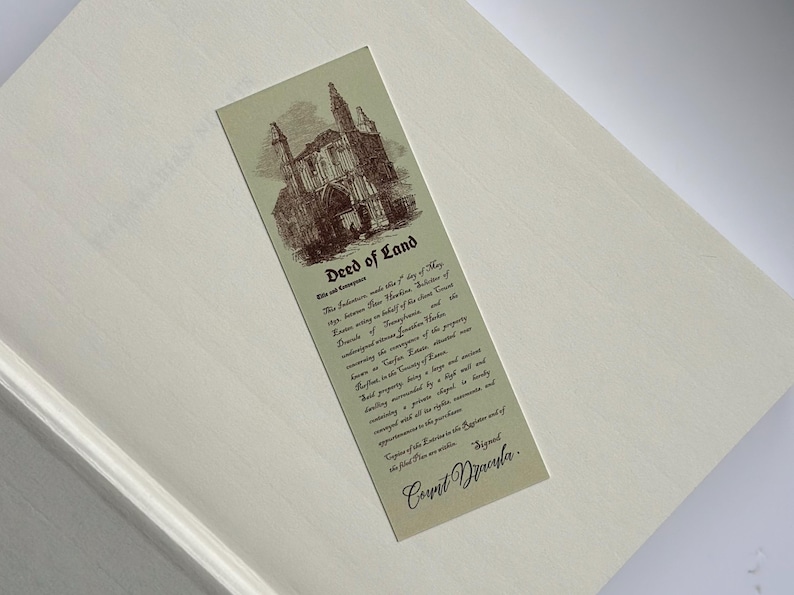 May include: A vintage-style bookmark with the text "Deed of Land" and an illustration of a building. The bookmark is rectangular, with a cream background and sepia-toned graphics and text. The text includes the signature "Count Dracula."