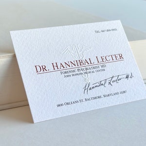 K&ouml;nnte beinhalten: Eine wei&szlig;e Visitenkarte mit gepr&auml;gtem Text und Unterschrift. Die Karte lautet "DR. HANNIBAL LECTER, FORENSIC PSYCHIATRIST MD, JOHN HOPKINS MEDICAL CENTER." Die Karte enth&auml;lt auch eine Telefonnummer und Adresse.