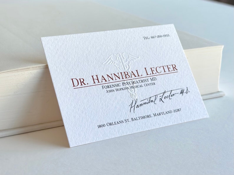 K&ouml;nnte beinhalten: Eine wei&szlig;e Visitenkarte mit gepr&auml;gtem Text und Unterschrift. Die Karte lautet "DR. HANNIBAL LECTER, FORENSIC PSYCHIATRIST MD, JOHN HOPKINS MEDICAL CENTER." Die Karte enth&auml;lt auch eine Telefonnummer und Adresse.