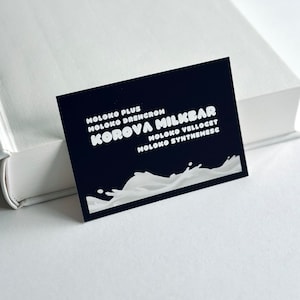 Puede incluir: Una tarjeta de visita negra con texto blanco que dice "Moloko Plus Moloko Drencrom Korova Milkbar Moloko Velloqet Moloko Synthemesc". La tarjeta tiene un diseño de onda blanca en la parte inferior.
