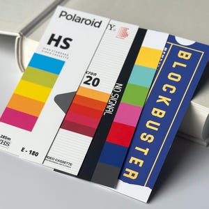 May include: A stack of retro-themed cards featuring VHS tape designs. The cards display the words "Polaroid", "HS", "cron 20", "NO SIGNAL", and "BLOCKBUSTER". The color palette includes vibrant hues of yellow, orange, pink, green, and blue.