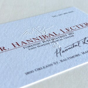 K&ouml;nnte beinhalten: Eine Visitenkarte mit dem Namen "Dr. Hannibal Lecter" in kastanienbraunen Buchstaben. Die Karte enth&auml;lt den Text "Forensic Psychiatrist MD" und "John Hopkins Medical Center". Eine Unterschrift und Adresse sind ebenfalls vorhanden.