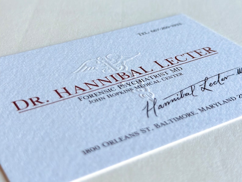 K&ouml;nnte beinhalten: Eine Visitenkarte mit dem Namen "Dr. Hannibal Lecter" in kastanienbraunen Buchstaben. Die Karte enth&auml;lt den Text "Forensic Psychiatrist MD" und "John Hopkins Medical Center". Eine Unterschrift und Adresse sind ebenfalls vorhanden.