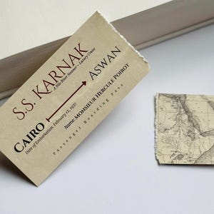 K&ouml;nnte beinhalten: Ein Vintage-Bordkarte f&uuml;r die S.S. Karnak Nilkreuzfahrt, mit Text, der Kairo nach Assuan anzeigt, datiert vom 12. Februar 1937, und eine Karte. Der Pass ist beige mit braunem Text. Der Name auf dem Pass ist Monsieur Hercule Poirot.