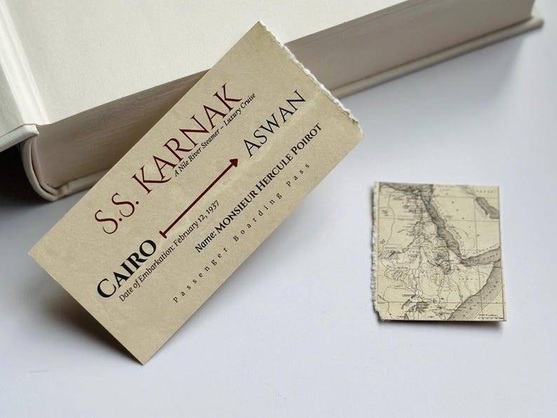 K&ouml;nnte beinhalten: Ein Vintage-Bordkarte f&uuml;r die S.S. Karnak Nilkreuzfahrt, mit Text, der Kairo nach Assuan anzeigt, datiert vom 12. Februar 1937, und eine Karte. Der Pass ist beige mit braunem Text. Der Name auf dem Pass ist Monsieur Hercule Poirot.