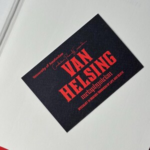 K&ouml;nnte beinhalten: Eine schwarze Visitenkarte mit rotem Text, der "VAN HELSING, Metaphysiker, Spezialist f&uuml;r obskure St&ouml;rungen des Lebens und des Todes" lautet. Die Karte enth&auml;lt auch den Text "Universit&auml;t von Amsterdam".