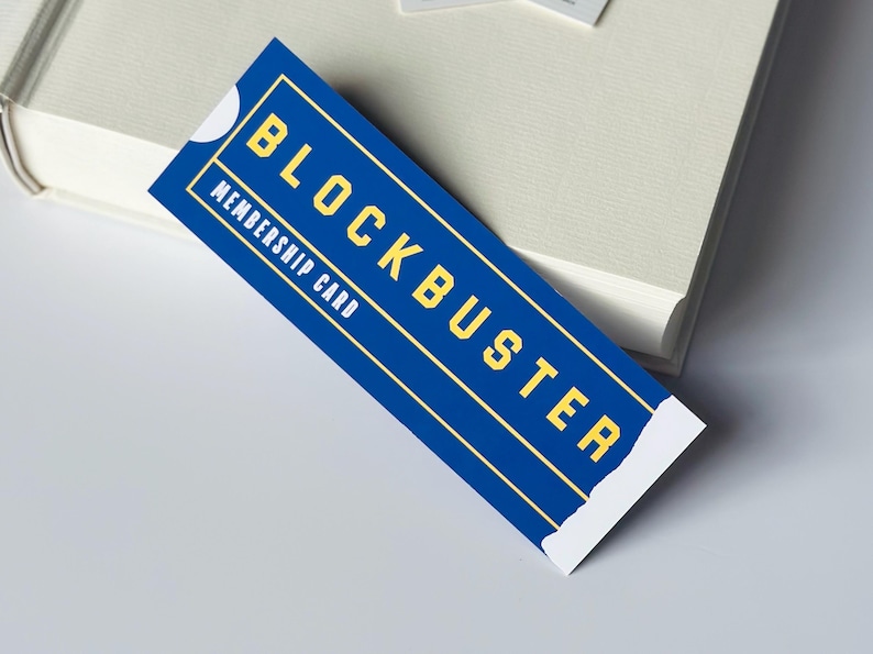 May include: A blue Blockbuster membership card with yellow text. The card reads "BLOCKBUSTER" and "MEMBERSHIP CARD". The card is rectangular with a white border and is placed on a white surface.