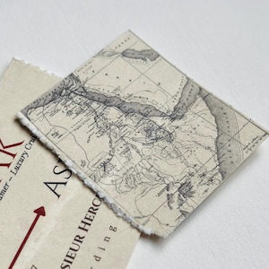 K&ouml;nnte beinhalten: Eine Vintage-Karte auf strukturiertem Papier mit detailliertem geografischem Layout. Die Karte ist in Grau- und Beiget&ouml;nen gehalten und hat einen zerrissenen Rand. Darunter befindet sich ein cremefarbenes Papier mit dem Wort "KARNAK" in Rot.
