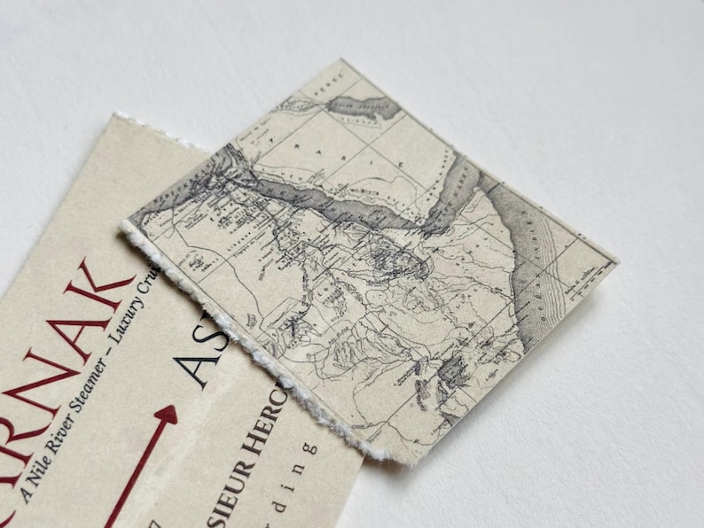 K&ouml;nnte beinhalten: Eine Vintage-Karte auf strukturiertem Papier mit detailliertem geografischem Layout. Die Karte ist in Grau- und Beiget&ouml;nen gehalten und hat einen zerrissenen Rand. Darunter befindet sich ein cremefarbenes Papier mit dem Wort "KARNAK" in Rot.