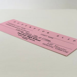 以下が含まれることがあります： ピンク色の居残り票で、上部に「DETENTION SLIP」と記載されています。票には「March 24th at 07:00am」と日付が記され、「Saturday」と「Shermer High School」と記載されています。票には生徒の氏名と、校長である「V.P. Vernon」の署名欄があります。