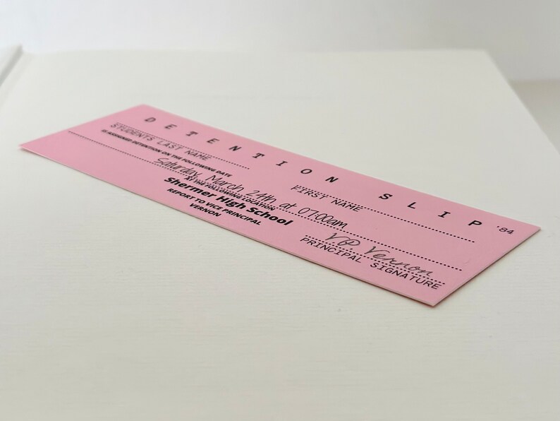 以下が含まれることがあります： ピンク色の居残り票で、上部に「DETENTION SLIP」と記載されています。票には「March 24th at 07:00am」と日付が記され、「Saturday」と「Shermer High School」と記載されています。票には生徒の氏名と、校長である「V.P. Vernon」の署名欄があります。