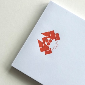 Op de afbeelding: Een wit vierkant met een rood geometrisch logo en de tekst "NAKATOMI PLAZA" in rood.