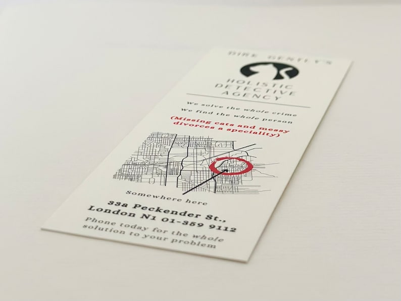 Op de afbeelding: Een zwart-witte visitekaartje met een rode cirkel rond een kaart van een stad. De tekst op de kaart luidt "Dire Sentes Holistic Detective Agency" en "We solve the whole crime. We find the whole person. (Missing cats and messy divorces a speciality)". De kaart bevat ook een adres en een telefoonnummer: "33a Peckender St., London N1 01-359 9112. Phone today for the whole solution to your problem."