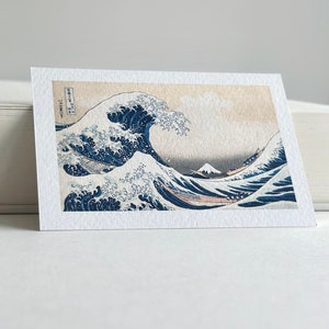 May include: A vintage Japanese woodblock print depicting a large blue wave crashing over a boat with Mount Fuji in the background. The print is titled "The Great Wave off Kanagawa" by Katsushika Hokusai.