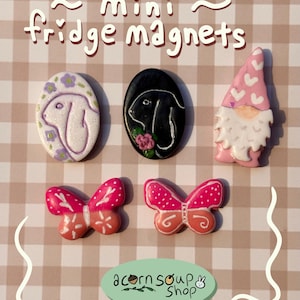 May include: Mini fridge magnets in various designs. Includes a white bunny with purple flowers, a black bunny with a pink flower, a pink gnome, and two pink and orange butterflies. The text "mini fridge magnets" is at the top.