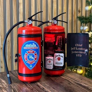 Może przedstawiać: Czerwony barek w kształcie gaśnicy z emblematem straży pożarnej Rochester, NY. Szafka ma czarny uchwyt i wąż. Otwarta szafka odsłania butelki bourbonu i coli Jim Beam. Czarne drzwi wyświetlają tekst.